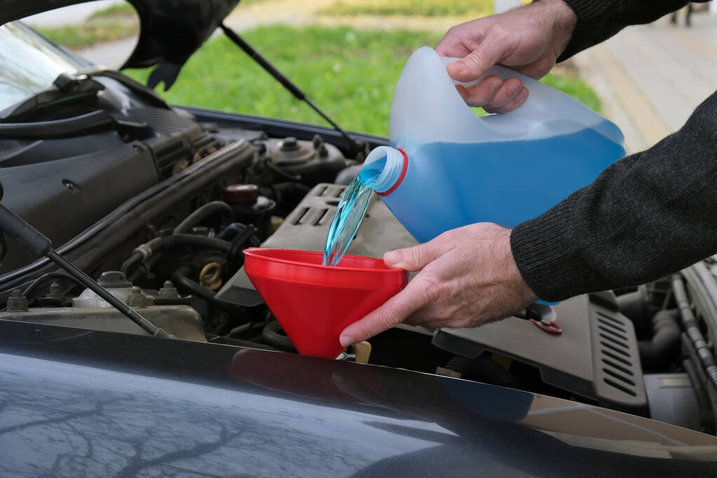 Tehniskie jautājumi 6 - Koni Autoskola - stock photo driver mechanic pouring windshield washer fluid car - Koni Autoskola -